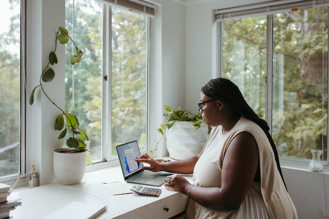 Person sitting at a desk in front of a window using a calculator and laptop